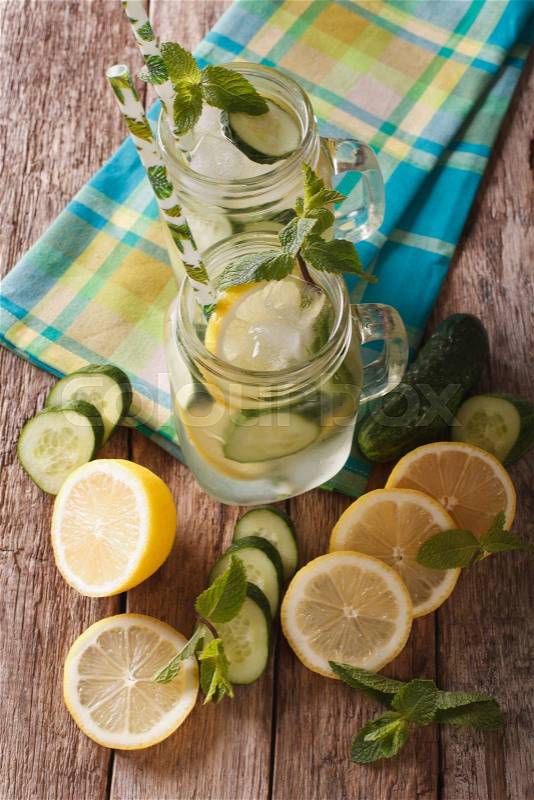 Cold water with cucumber, lemon, ice and mint close up in a glass jar on the table. vertical view from above\, stock photo