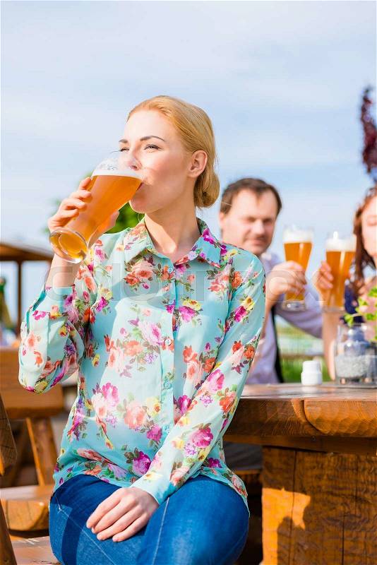 Woman drinking with friends in beer garden, stock photo