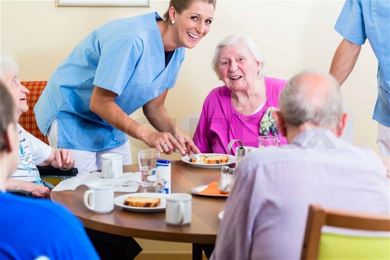 Group of seniors having food in nursing home, a nurse is serving, stock photo
