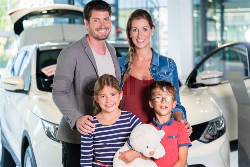 Family with children buying new car at auto dealership, mom, dad and kids standing in showroom, stock photo