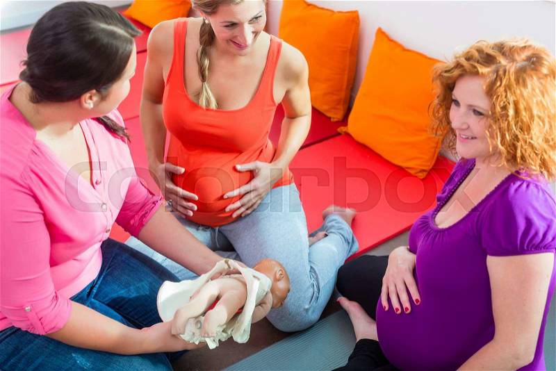 Midwife explaining birth process to pregnant women during antenatal class with anatomic model of pelvic bone, stock photo