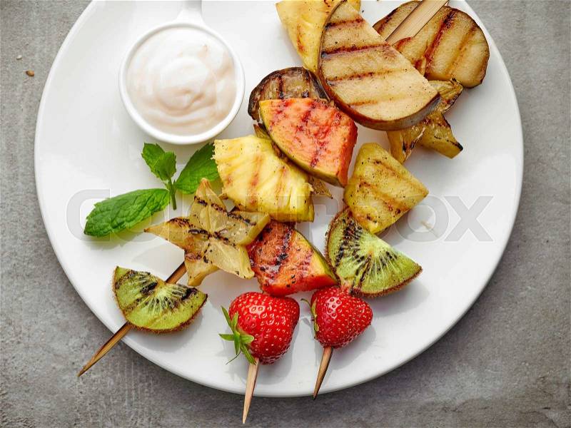 Grilled fruits on wooden skewers and yogurt sauce, top view, stock photo