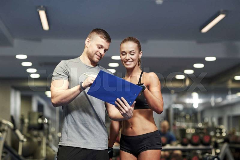 Fitness, sport, exercising and diet concept - smiling young woman and personal trainer with clipboard writing exercise plan in gym, stock photo