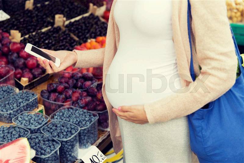 Sale, shopping, food, pregnancy and people concept - close up of pregnant woman with smartphone and shopper bag at street market, stock photo
