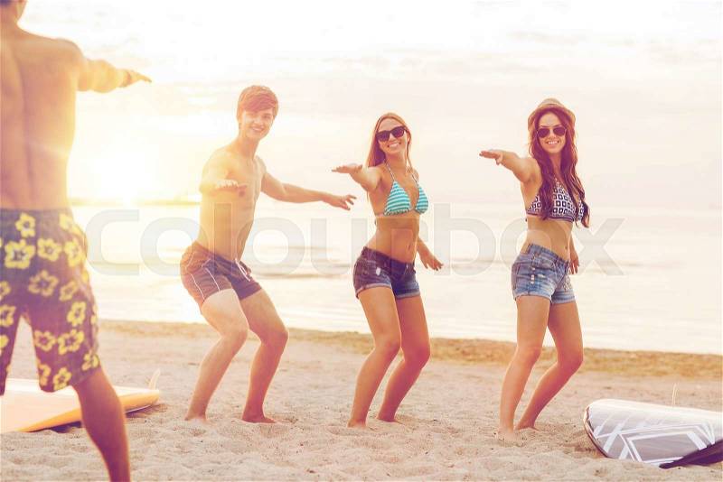 Friendship, sea, summer vacation, water sport and people concept - group of smiling friends wearing swimwear and sunglasses with surfboards on beach, stock photo