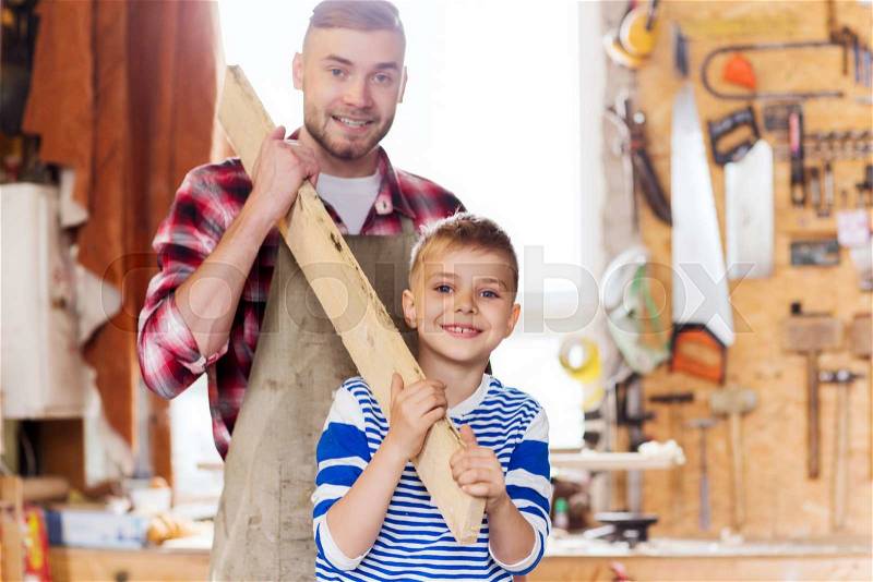 Family, carpentry, woodwork and people concept - happy father and little son carrying wood plank at workshop, stock photo