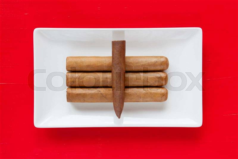 White ceramic dish with luxury Cuban cigars on over red background, rectangle dish, stock photo