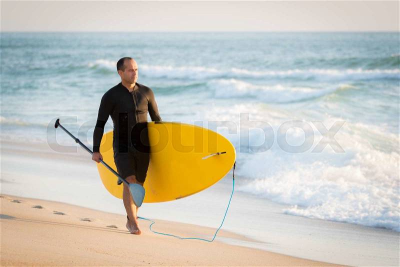 Man with his paddle board on the beach at sunset, stock photo