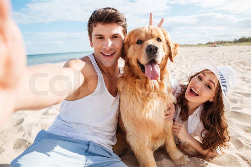 Young happy couple with dog taking a selfie at the beach, stock photo