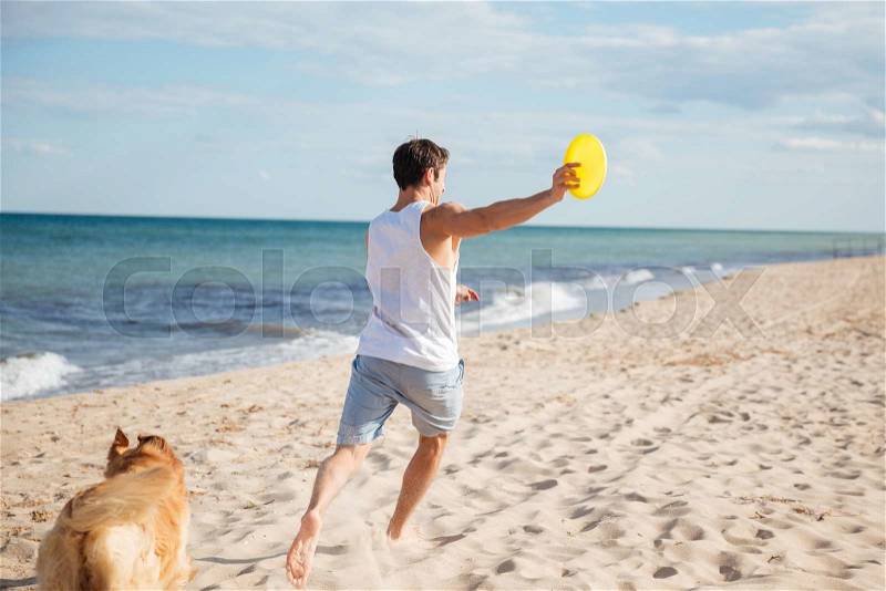 Young athletic handsome man playing with his dog on the beach, stock photo
