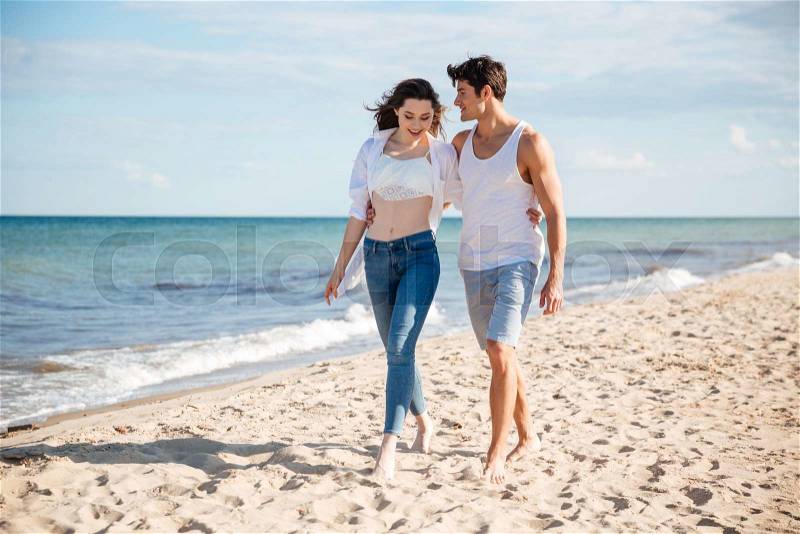 Beautiful young couple talking and walking on the beach together, stock photo