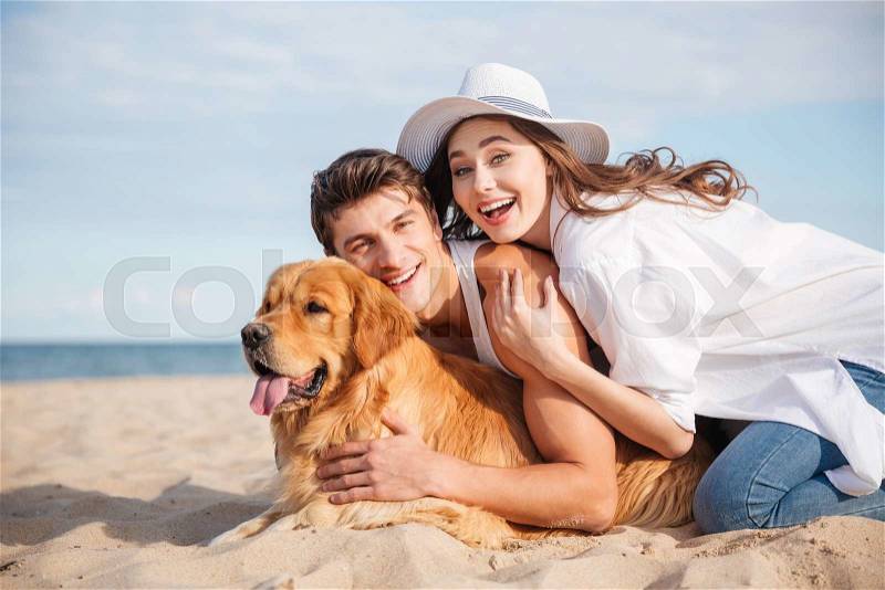 Happy young couple with dog laughing and having fun together on the beach, stock photo