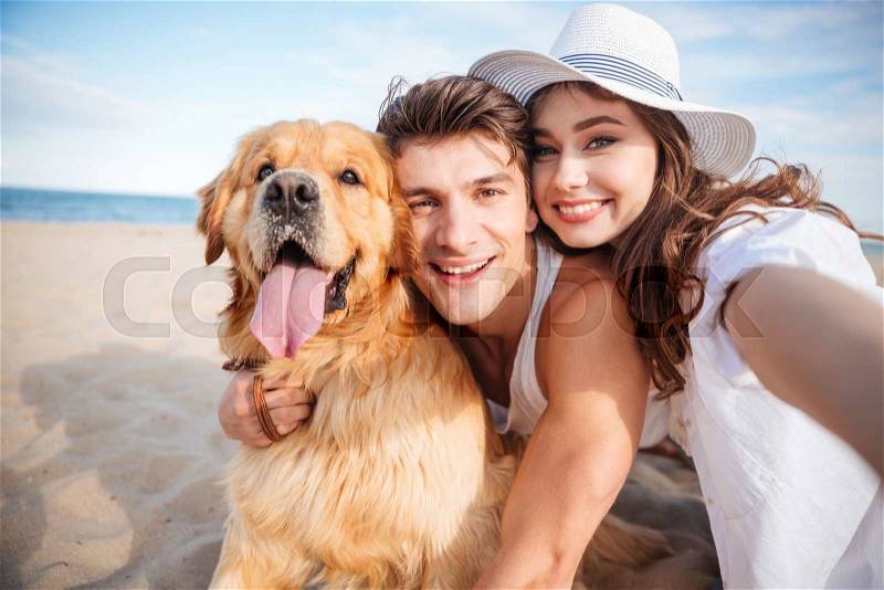 Portrait of happy young couple hugging their dog and smiling on the beach, stock photo