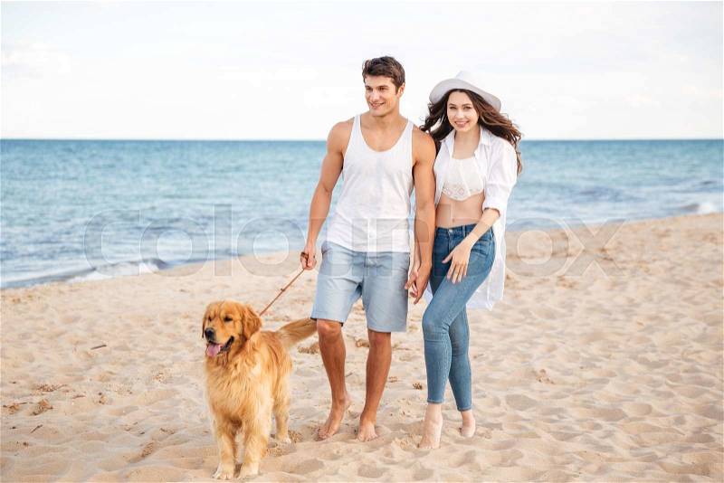 Romantic young beautiful couple walking on the sea shore with dog, stock photo