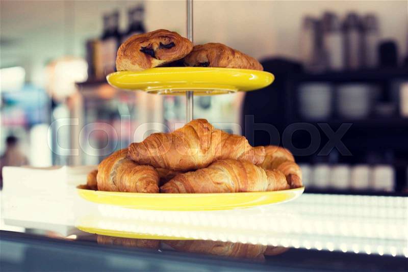 Food, baking, junk-food and unhealthy eating concept - close up of croissants and buns on cake stand at cafe or bakery, stock photo