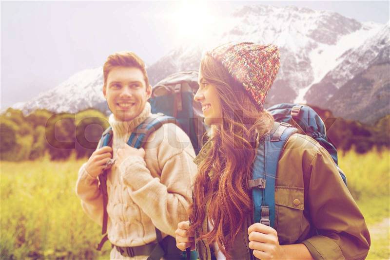 Adventure, travel, tourism, hike and people concept - smiling couple walking with backpacks over alpine mountains and hills background, stock photo