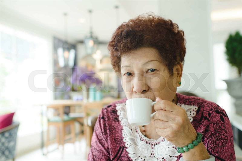 Happy Asian senior woman drinking tea at cafe, stock photo