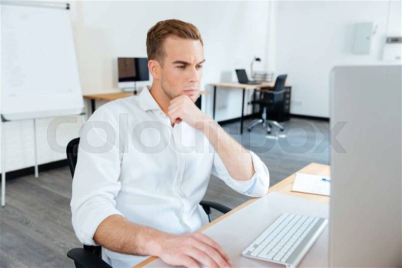 Thoughtful young businessman thinking and using computer at work, stock photo