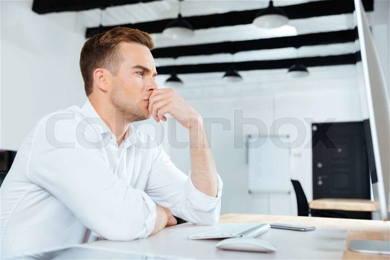 Pensive young businesman working with computer and thinking at workplace, stock photo