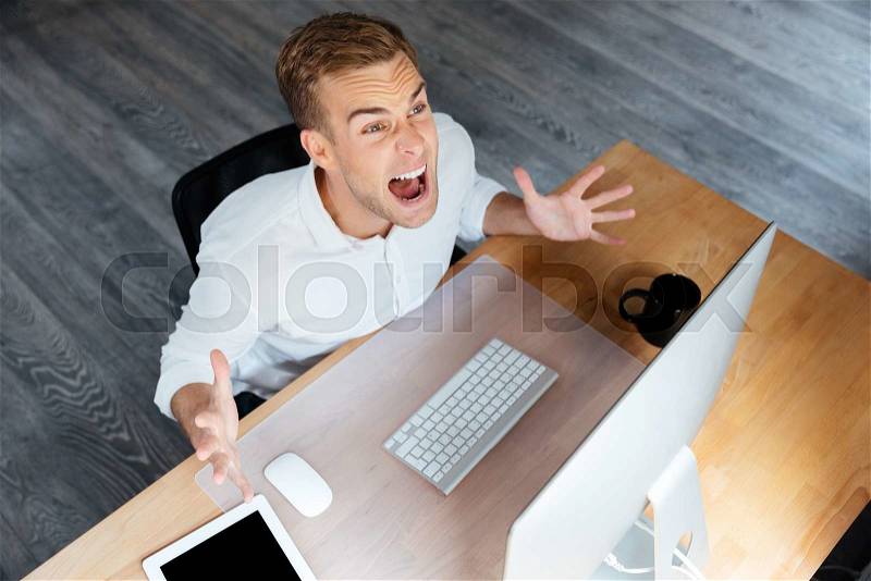 Top view of mad young businessman working with computer and shouting, stock photo