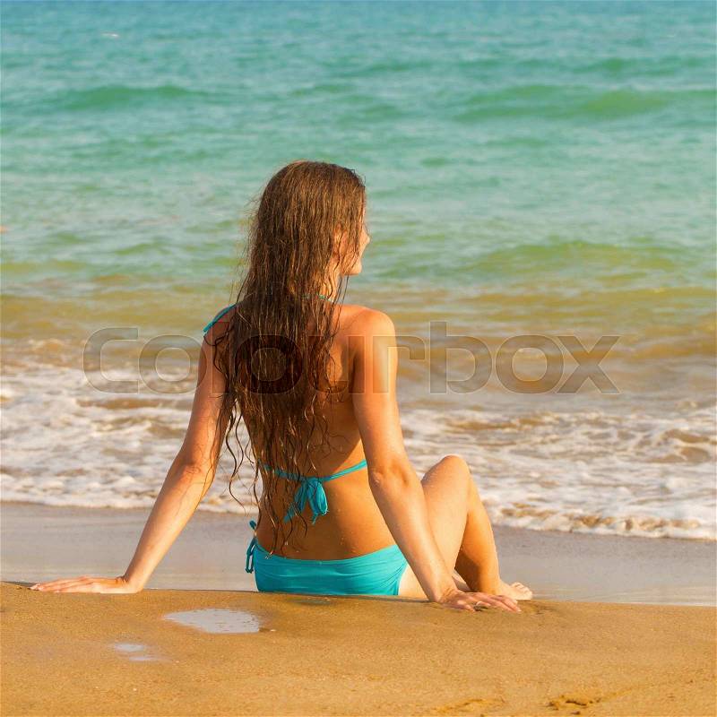 Woman sitting on seacoast in the surf line. Summer holidays concept, stock photo