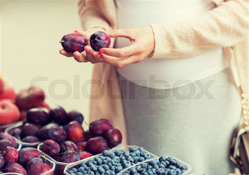 Sale, shopping, pregnancy and people concept - close up of pregnant woman choosing plums at street food market, stock photo