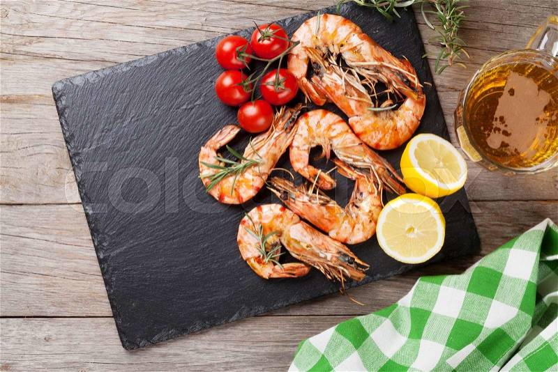Grilled shrimps on stone plate and beer mug on wooden table, stock photo