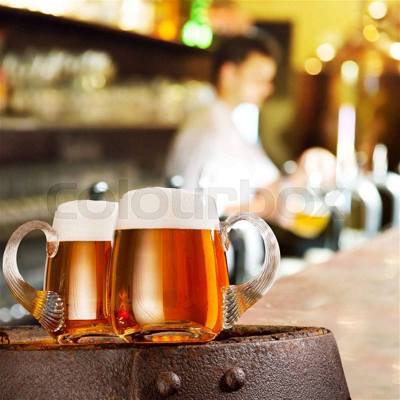 Two glasses of beer on the wooden barrel in the bar, stock photo