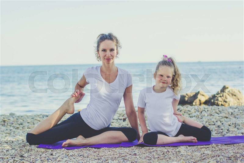 Smiling mother and child girl are doing yoga on the sea coast, stock photo