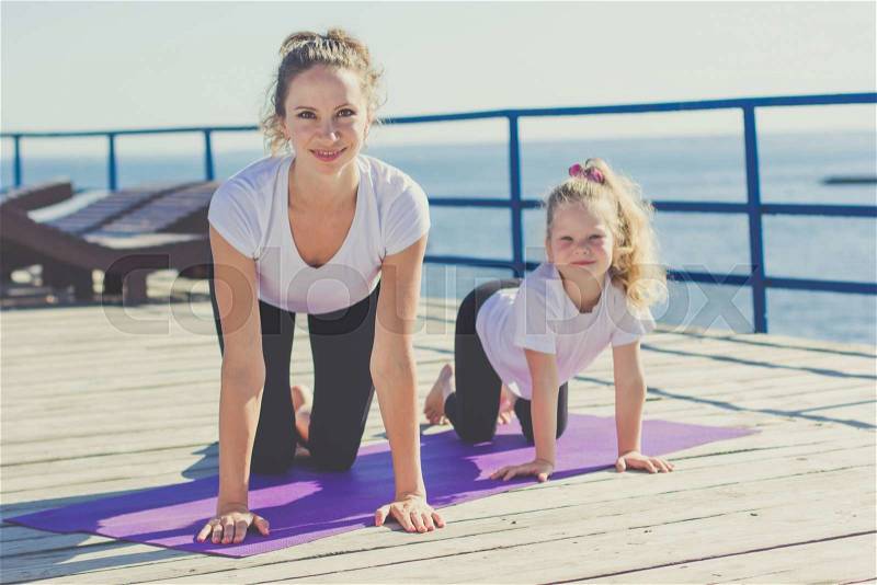 Smiling mother and child girl are doing yoga on the beach, stock photo
