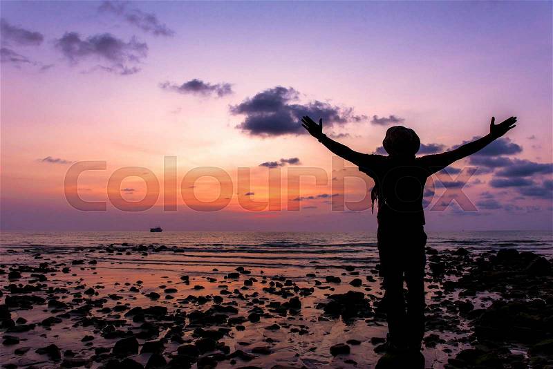Silhouette of traveler with hands up in the sunset on the ocean, stock photo