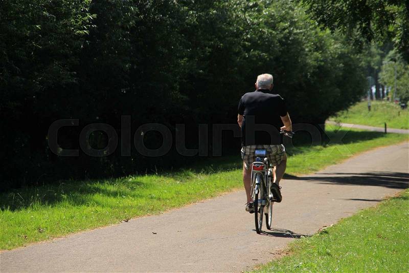 The solitary man in black shirt and short pants is biking in the park in the wonderful summer, stock photo