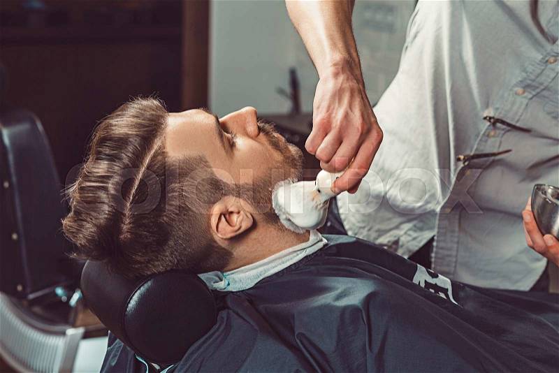 Hipster client visiting barber shop. The hands of young barber making the cut of beard, stock photo
