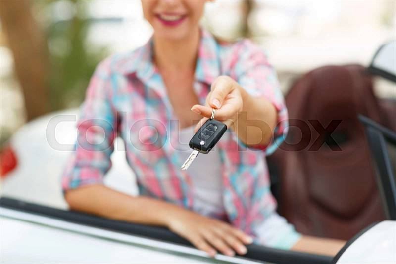Young pretty woman standing near convertible with keys in hand - concept of buying a used car or a rental car, stock photo