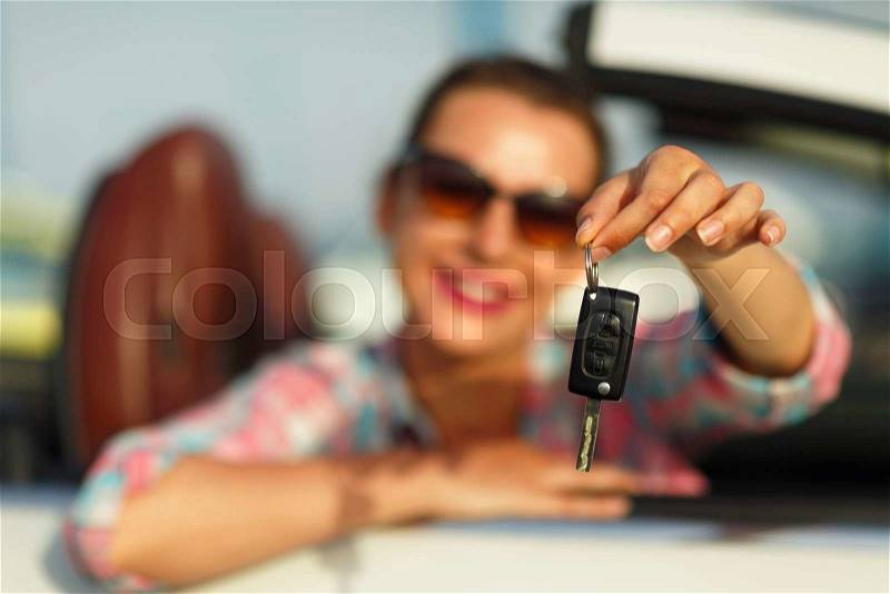 Young pretty woman sitting in a convertible car with the keys in hand - concept of buying a used car or a rental car, stock photo