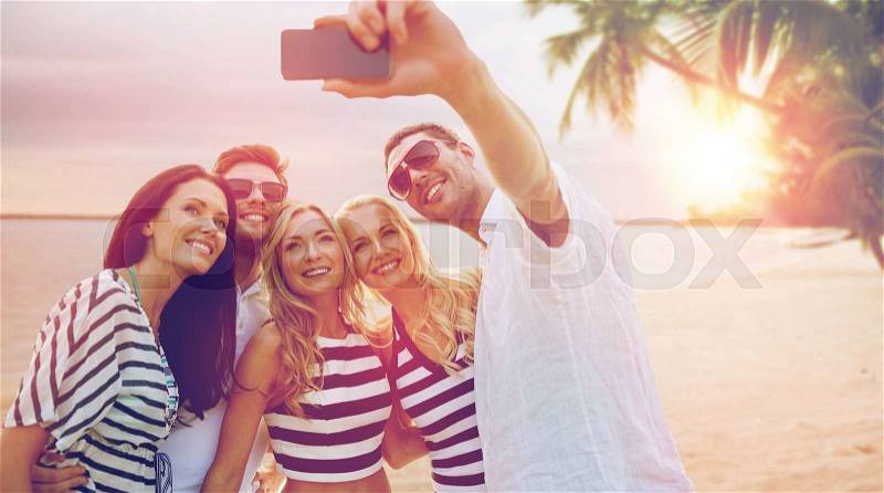 Summer holidays, travel, tourism, technology and people concept - group of smiling friends with smartphone photographing and taking selfie over exotic tropical beach background, stock photo