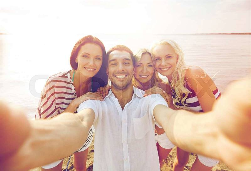 Summer, sea, tourism, technology and people concept - group of smiling friends with camera on beach photographing and taking selfie, stock photo