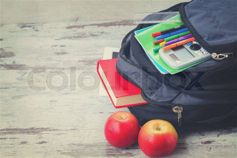 School backpack with supplies and apples on white desktop, retro toned, stock photo