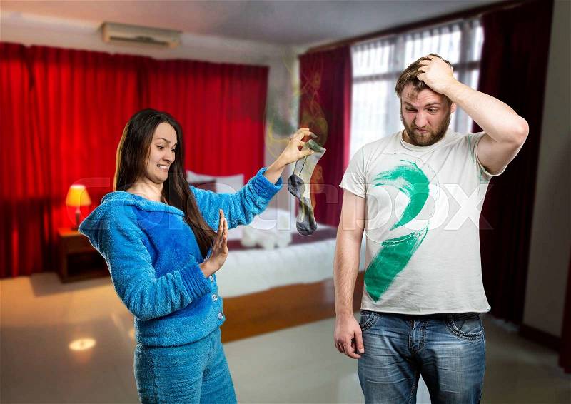 Disgusted woman holding a dirty sock of her husband at home, stock photo