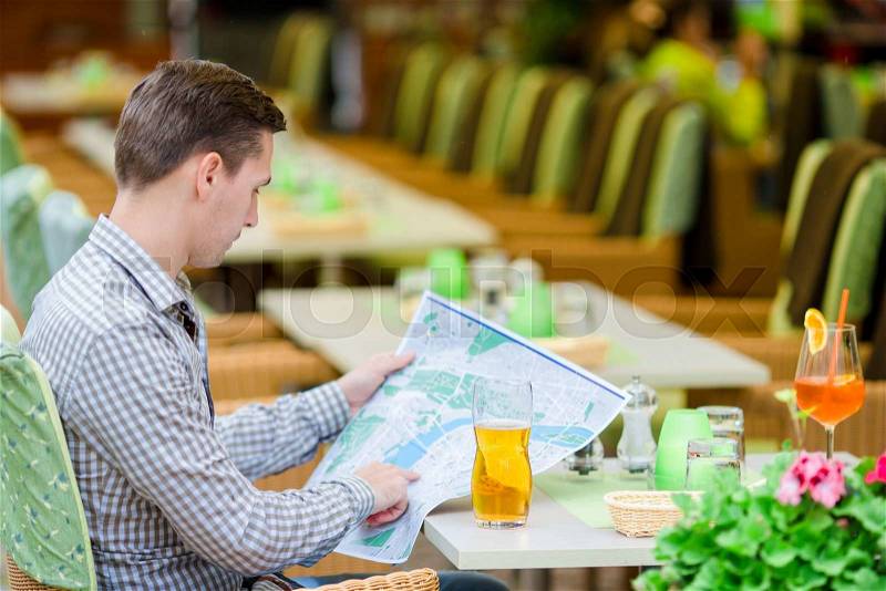Caucasian young european man with citymap in outdoors cafe. Portrait of attractive young tourist on lunch time, stock photo