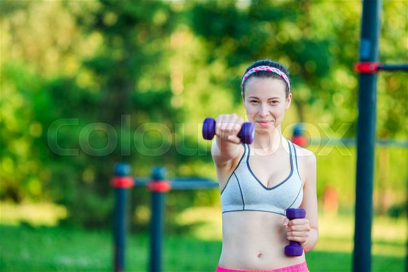Beautiful young woman working out with weights outdoors. Active girl working out with small dumbbells in the park, stock photo