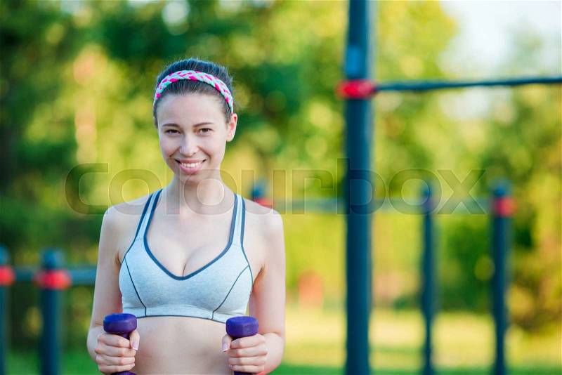 Beautiful young woman working out with weights outdoors. Active girl working out with small dumbbells in the park, stock photo