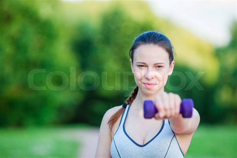 Fit young woman working out with weights outdoors. Active girl working out with small dumbbells in the park, stock photo