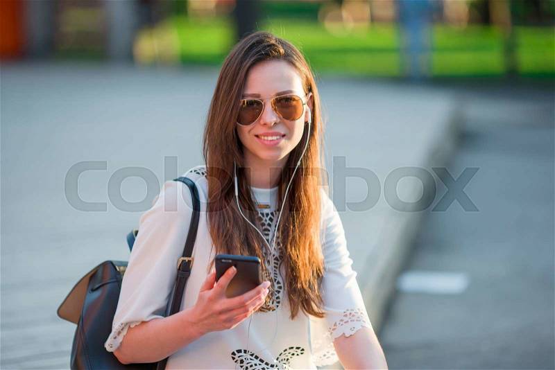 Tourist girl listening music by smartphone on summer holidays. Young attractive tourist with mobile phone outdoors enjoying holidays travel destination in tourism and exploring concept, stock photo