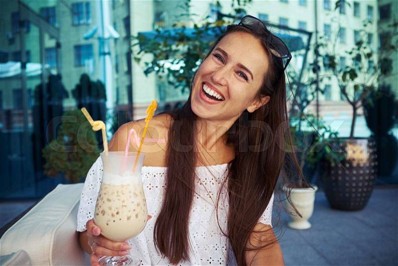 Cheerful young lady is having a good time in café in downtown drinking cocktail on open terrace, stock photo