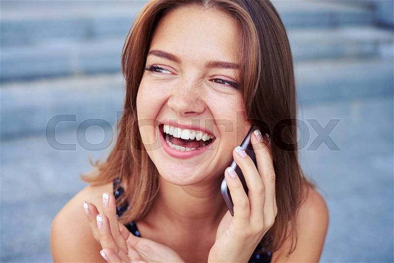 Happy young beautiful woman is laughing while talking on the phone on the street on a warm day, stock photo