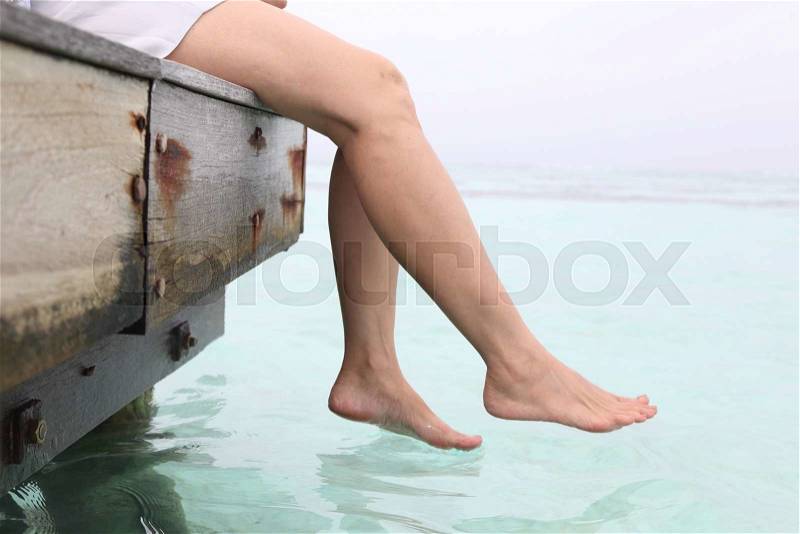 Woman\'s legs hanging into the sea on wooden pier, stock photo