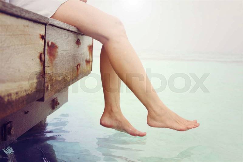 Woman\'s legs hanging into the sea on wooden pier, stock photo