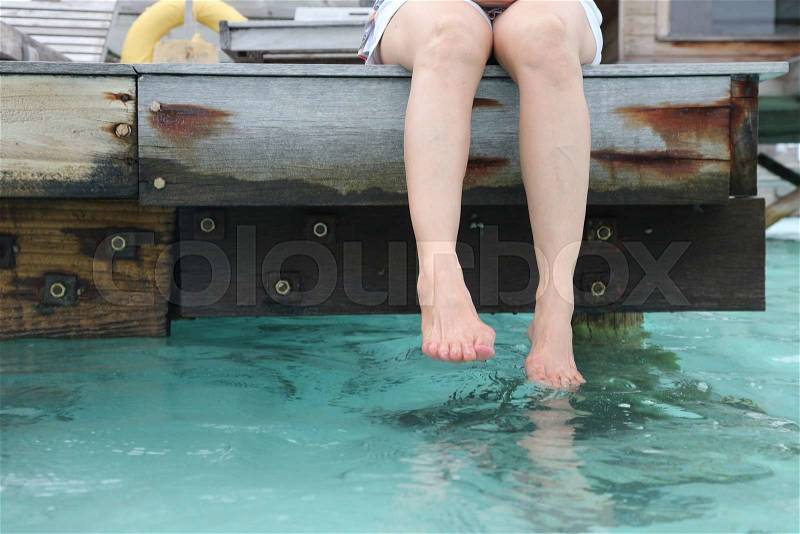 Woman's legs hanging into the sea on wooden pier, stock photo