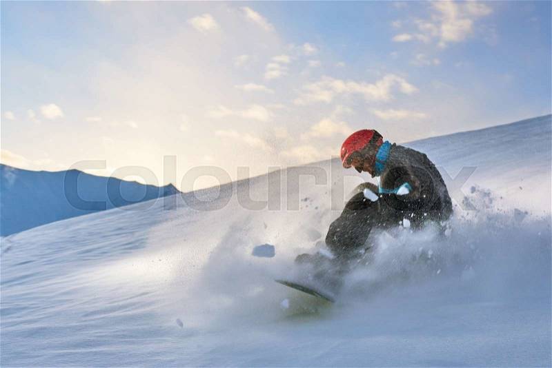 Girl snowboarder slows down the slope on a background of sunset sky, snow splashes, stock photo